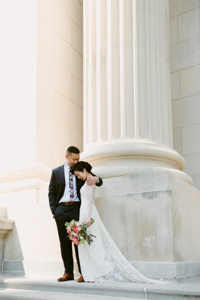 beautiful bride and groom standing under a giant pillar