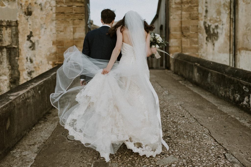 bride and groom walking along cobblestone path towards a castle