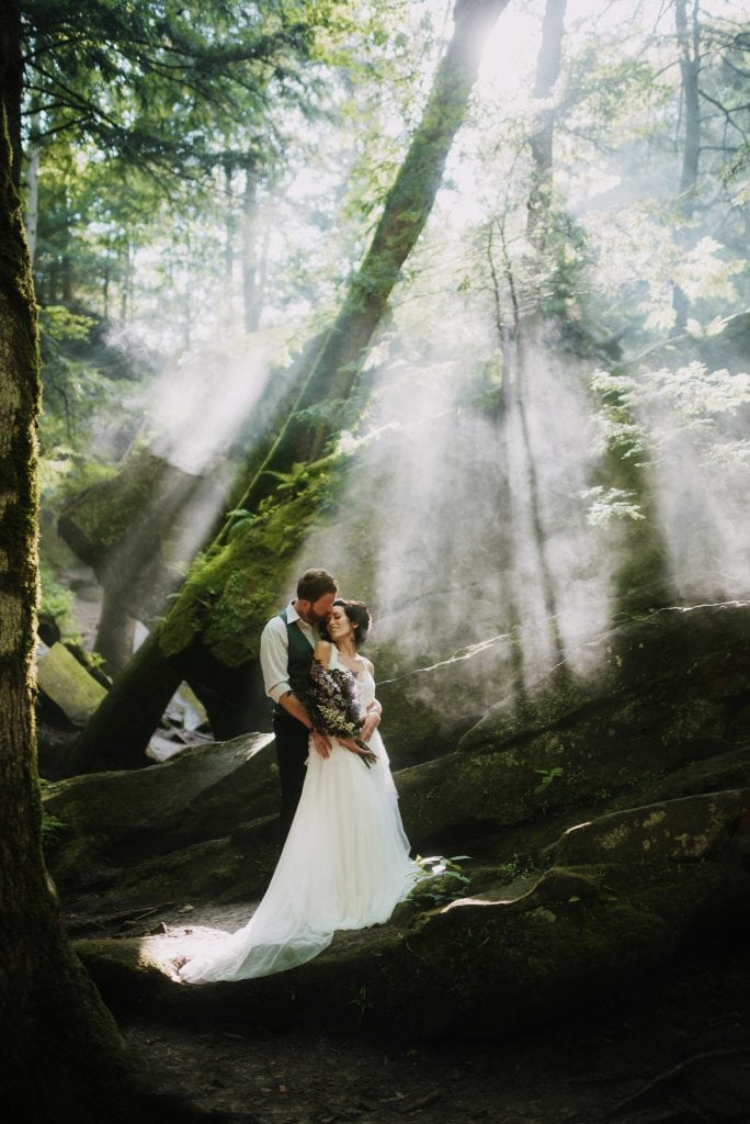 Beautiful bride and groom standing on rocks with sun shining