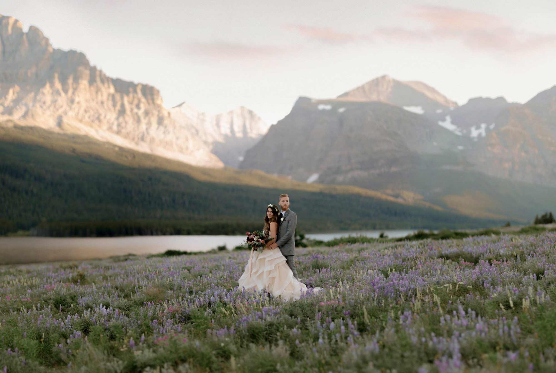 Bride and groom standing in a field of flowers amongst mountains